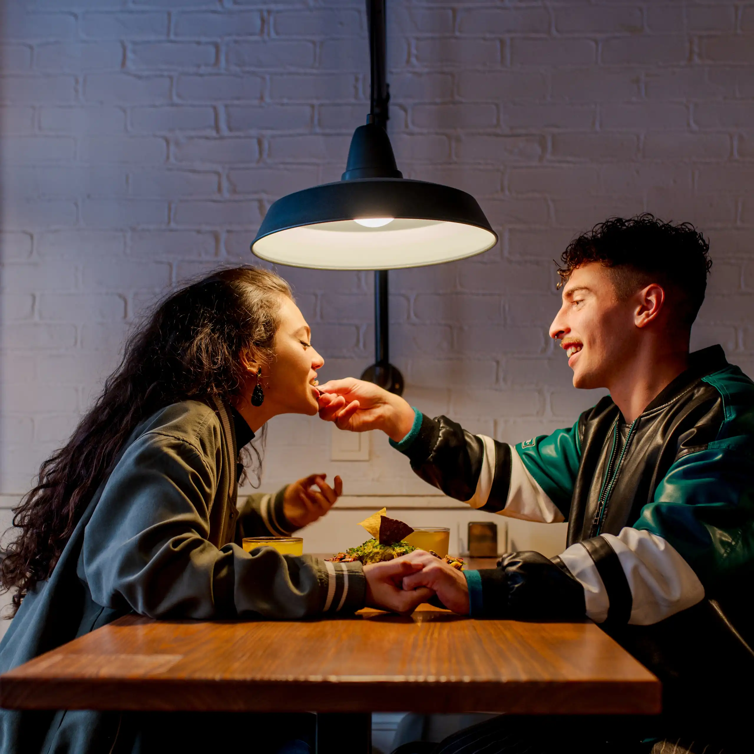 Un jeune couple partageant un repas intime ; un homme se penche au-dessus de la table pour toucher la lèvre inférieure de sa petite amie.