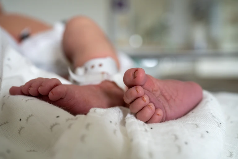 A newborn baby's feet wrapped on a white blanket. The baby wears a hospital identification ankle bracelet.