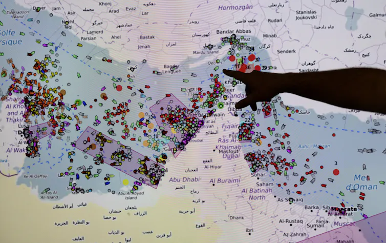A man points at a screen with a map of the Strait of Hormuz.