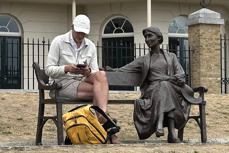 A person in ballcap sitting next to a statue of a woman who smiles benevolently.