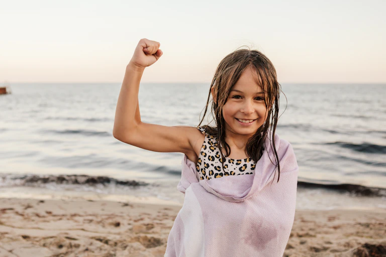 young girl flexing her right arm at the beach