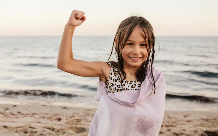 young girl flexing her right arm at the beach