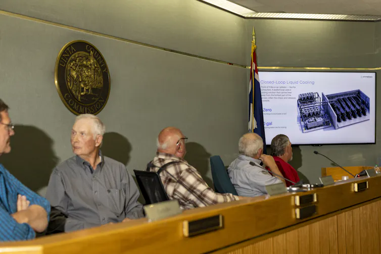People sit behind a long desk looking at a diagram of a data center cooling system.
