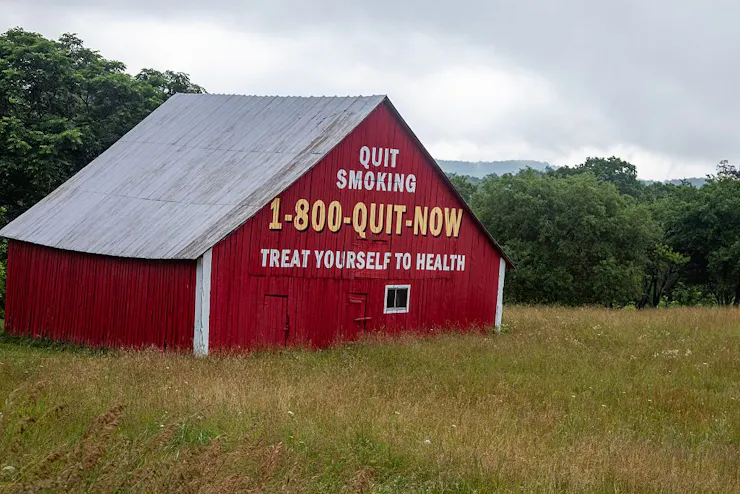 Red barn in a field with the words 'QUIT TOBACCO 1-800-QUIT-NOW TREAT YOURSELF TO HEALTH' painted on one side