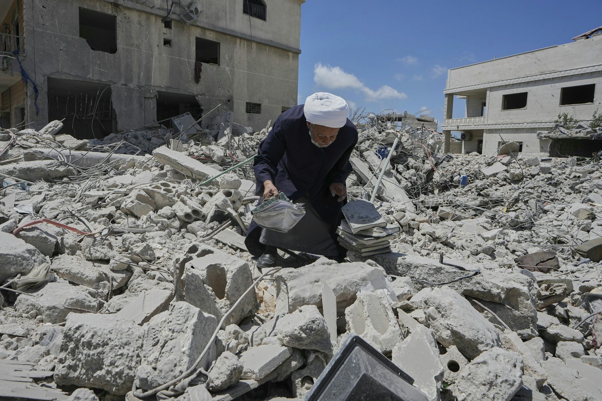 Un hombre se agacha entre las ruinas del bombardeo con una pila de libros.