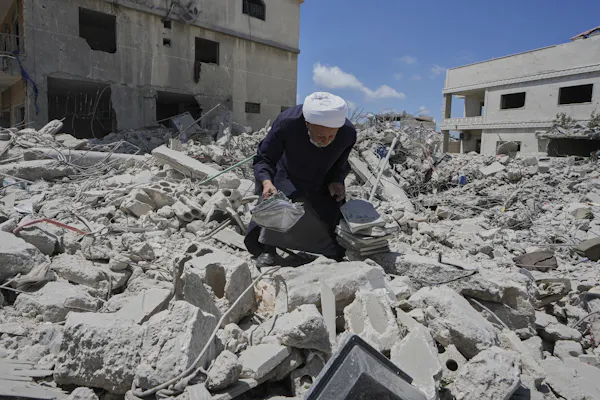 A man crouches in the rubble of bombing with a pile of books.
