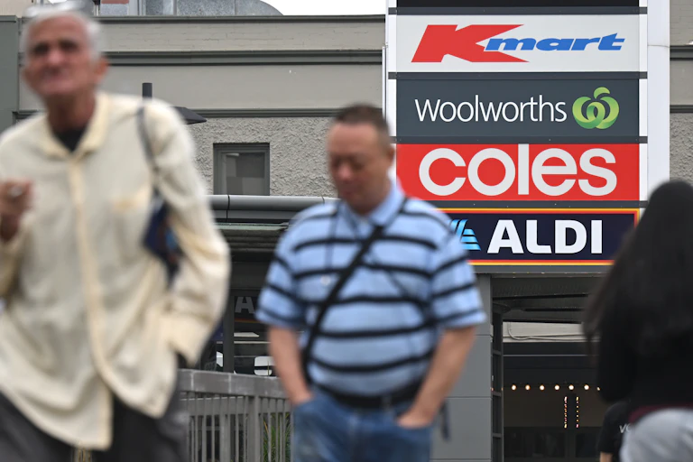 Shoppers walk past signs of Kmart, Woolworths, Coles and Aldi at a shopping precinct