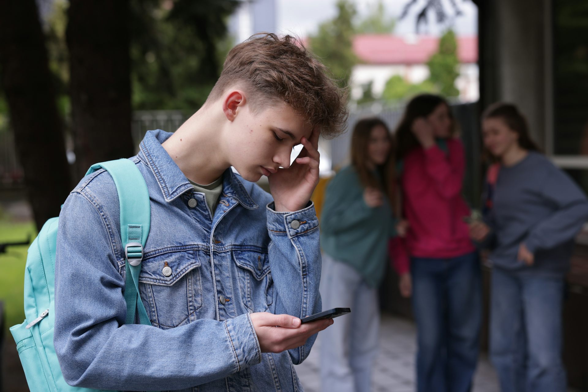 Boy on smartphone with talking girls in the background