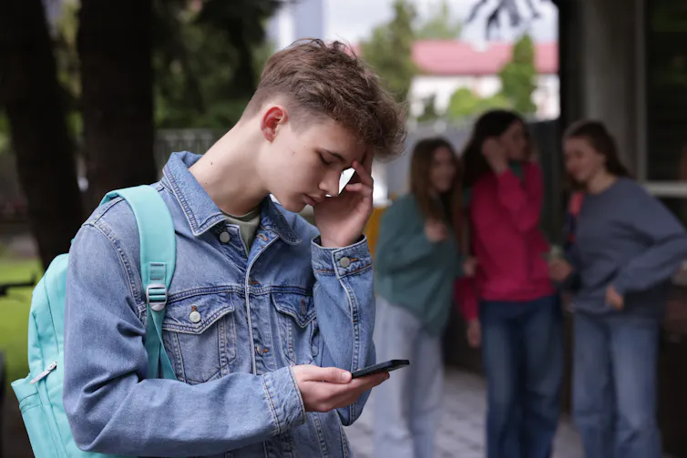 Boy on smartphone with talking girls in the background
