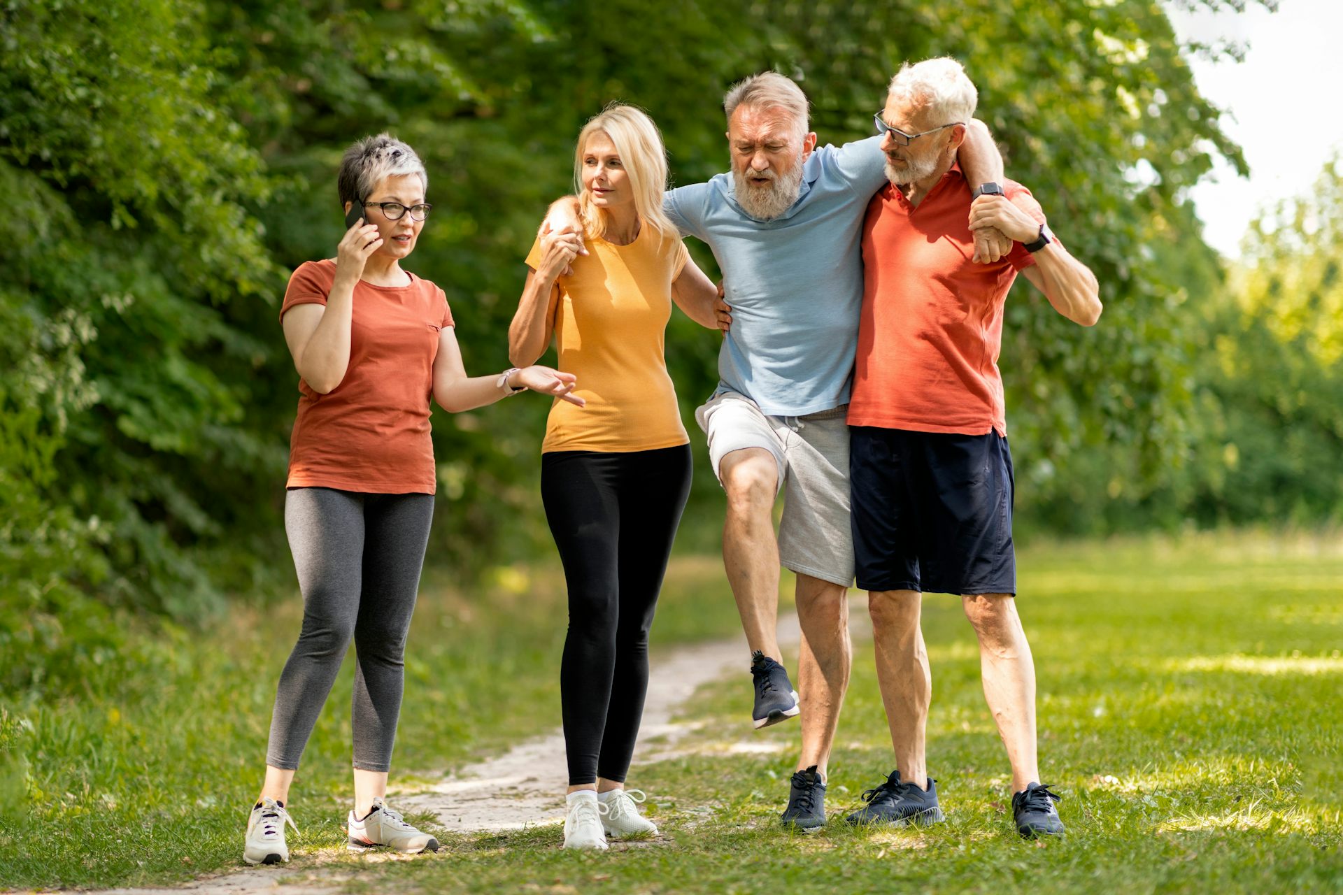 A group of elderly people wearing sports clothes support one man who has become injured. He is holding his foot up in pain.