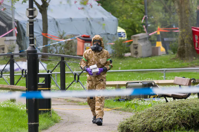 A soldier in a gas mask walks behind a police cordon.