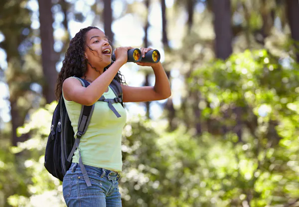 girl in summer clothes, smiling, holding binoculars in woods