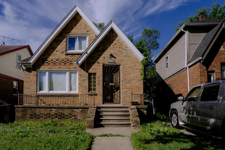 A small yellow-brick Craftsman bungalow sits in a dense neighborhood.