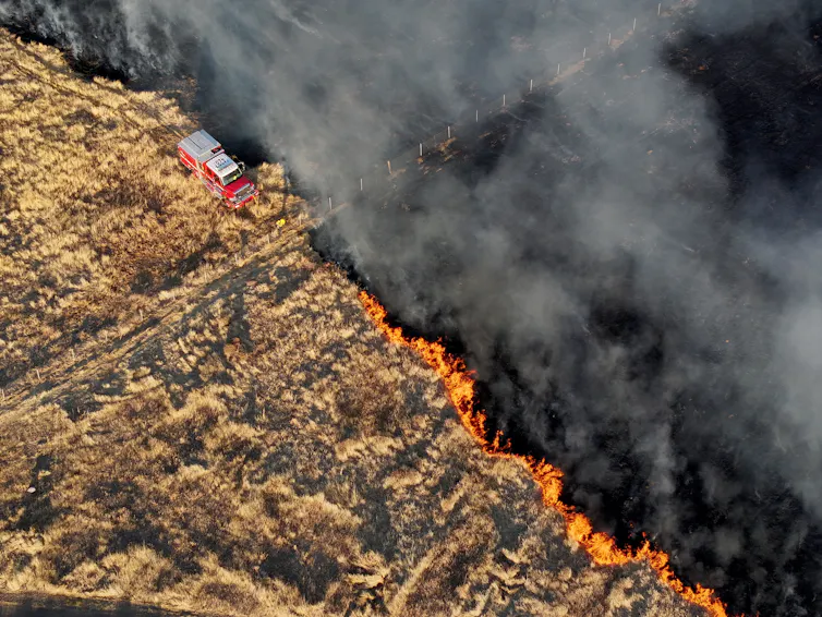 A fire trucks works at the edge of a spreading grass fire
