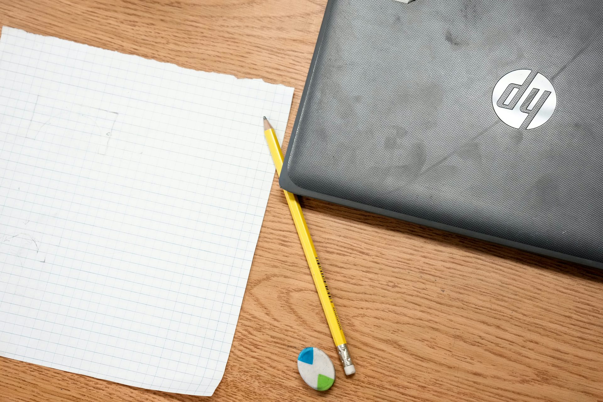 A laptop next to a pencil, eraser and lined paper on a school desk.