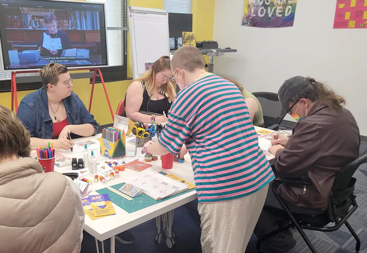 Las revistas DIY ayudan a las comunidades queer a contar sus historias y crear su propia cultura. 1 Las mujeres jóvenes se sientan alrededor de una mesa con papeles, marcadores y otras herramientas.