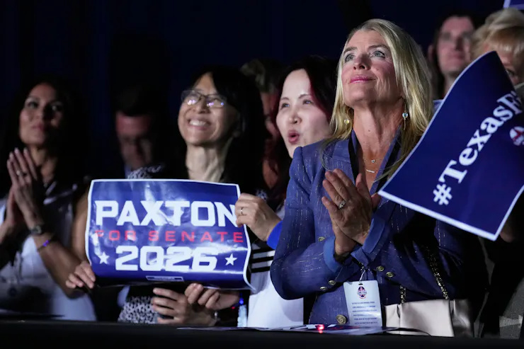 Several women hold signs and look toward a stage.