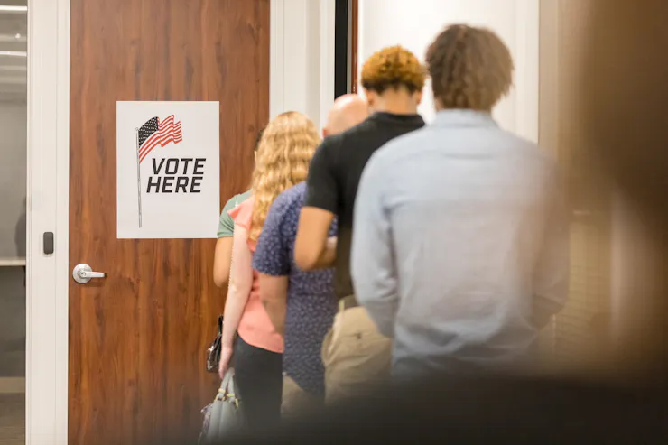 A rear view of a multiracial group of people standing in a long line in order to vote in the election.