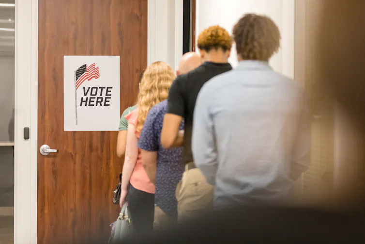 A rear view of a multiracial group of people standing in a long line in order to vote in the election.