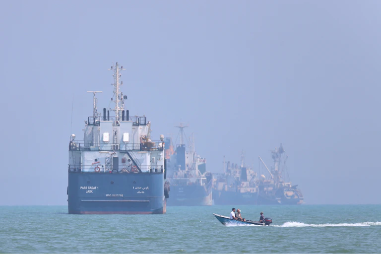 A small motorboat passes giant shipping vessels
