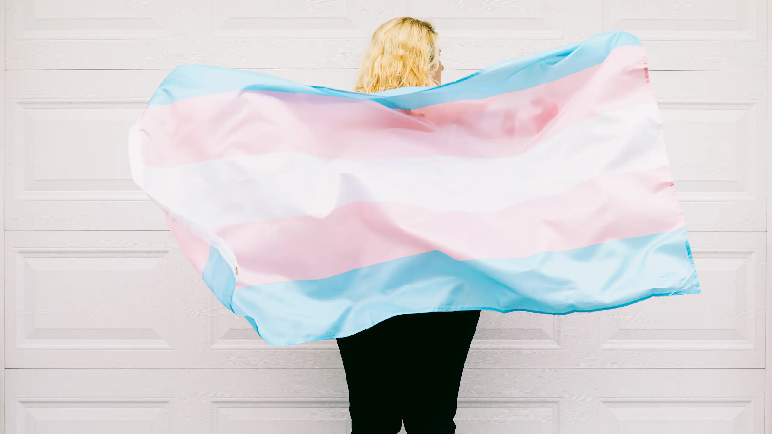 A person pictured from behind, with a trans flag
