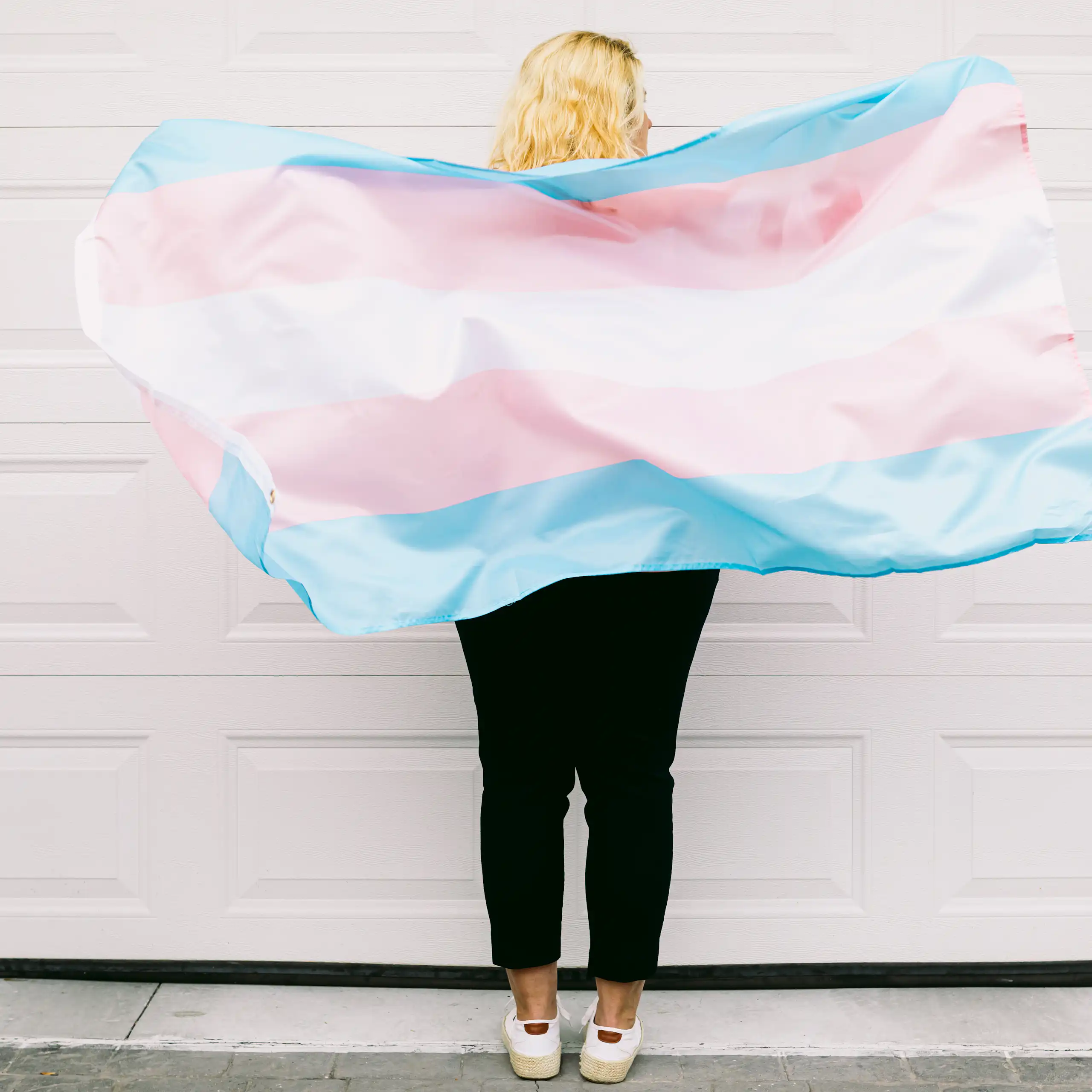 A person pictured from behind, with a trans flag