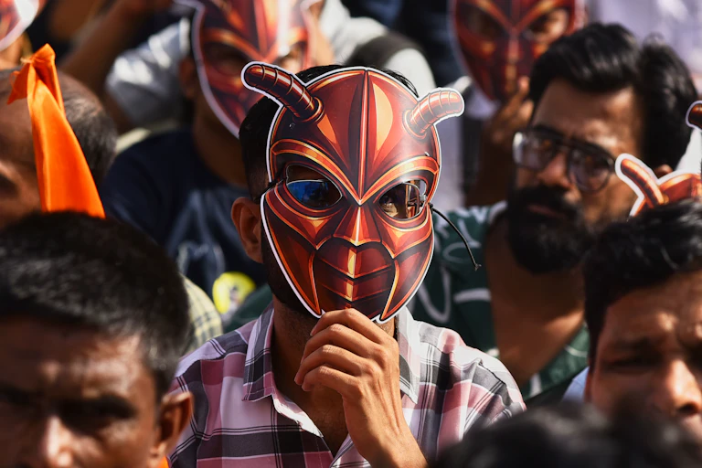 A man wearing a cardboard face mask of a red cockroach stands in a crowd of protesters.