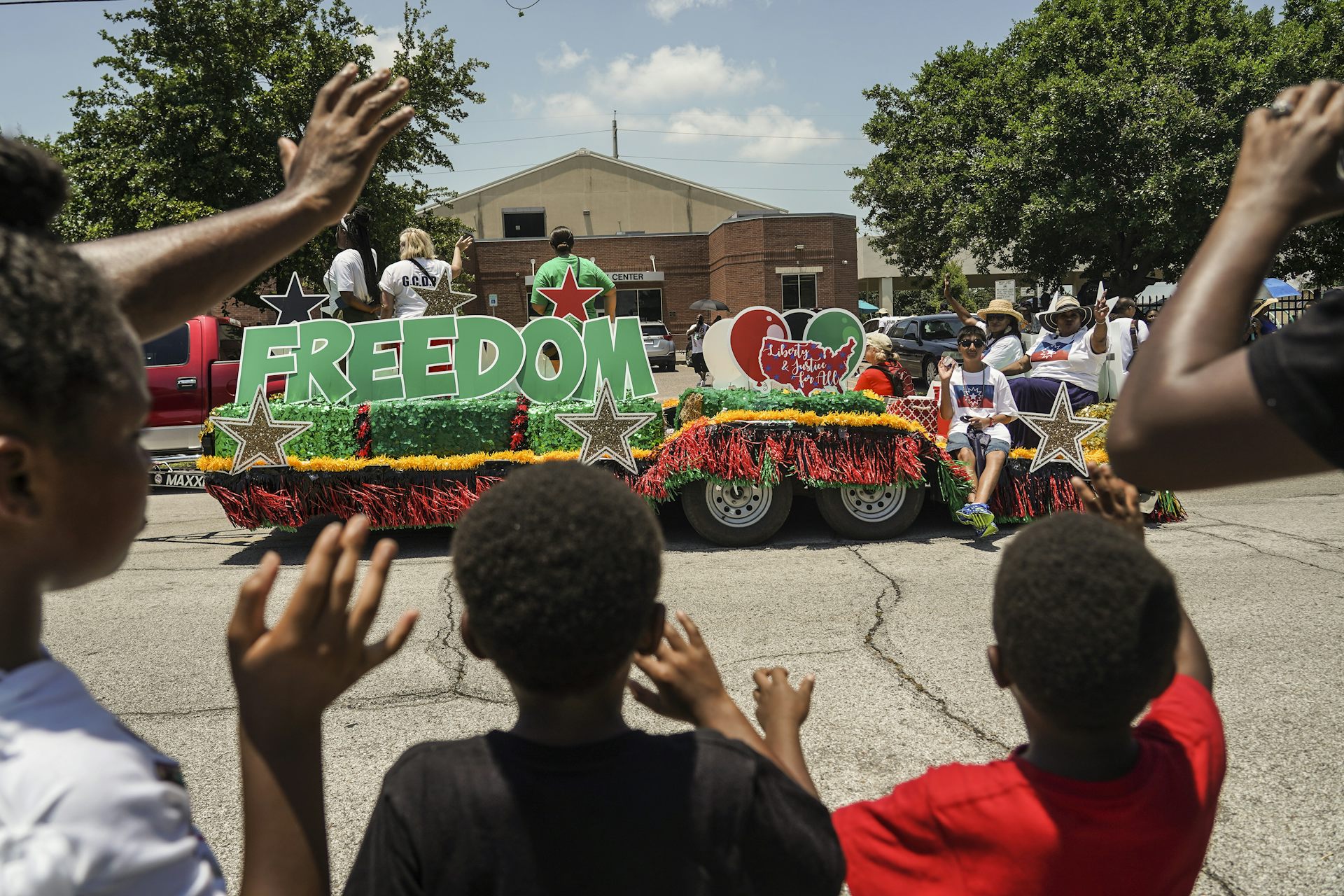 Black youth wave and cheer at a parade float.
