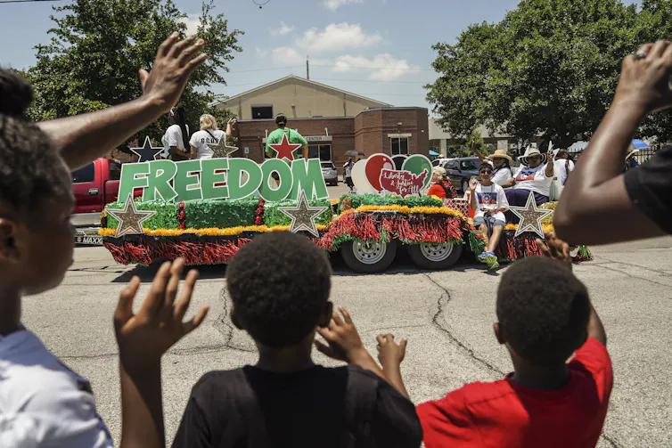 Black youth wave and cheer at a parade float.