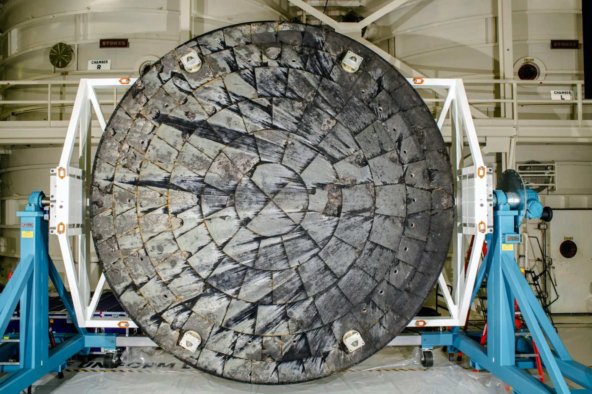A large circular shield, with some charring and peeling, sitting inside a warehouse