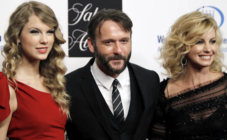 Two women (left and right) in fancy dresses and a man (centre) in a suit smile and pose for a photo.