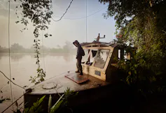A man stands on a small metal boat looking at a misty lake