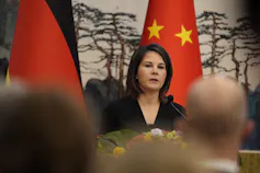 A dark-haired woman sits in front of a Chinese flag.