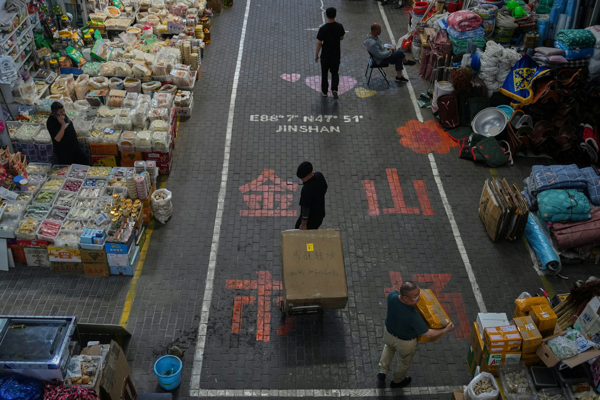 Vendors walk past shops at an outdoor market.