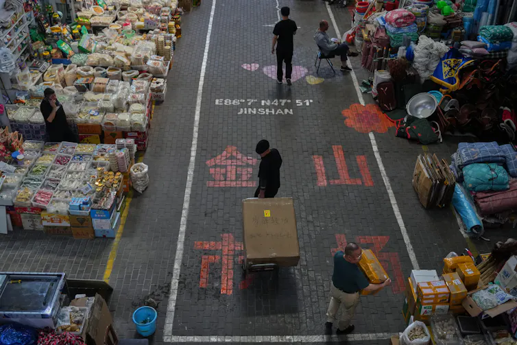 Vendors walk past shops at an outdoor market.