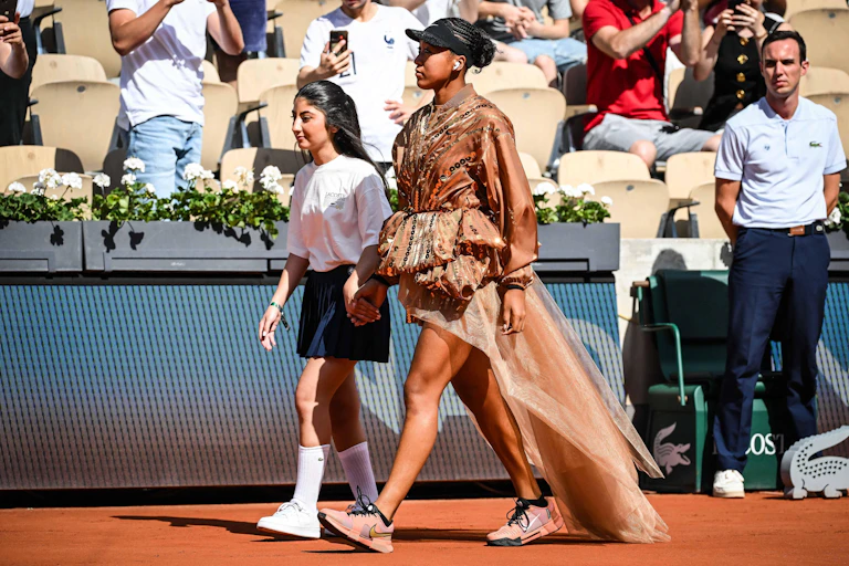 A young black tennis player wearing an elaborate fashion outfit on court.