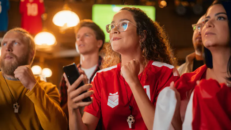 People in bar watching football and holding phones.