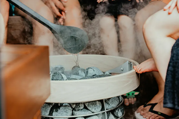 Poêle de sauna avec des pierres chaudes, de la vapeur et des gens assis autour