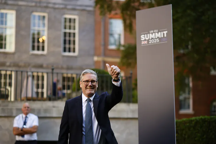 keir starmer with a thumb up in front of a sign reading Uk-EU summit 2025