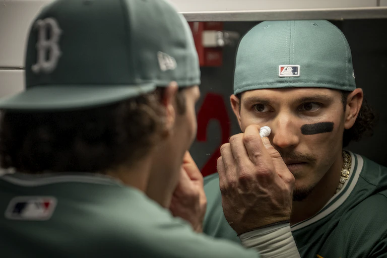A baseball player with cap on looks in the mirror and applies eye black.