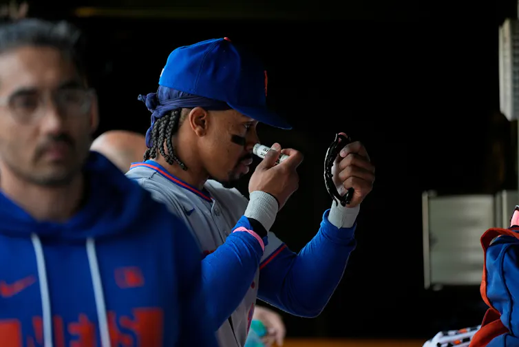 Black baseball player applies eye black with a handheld mirror.