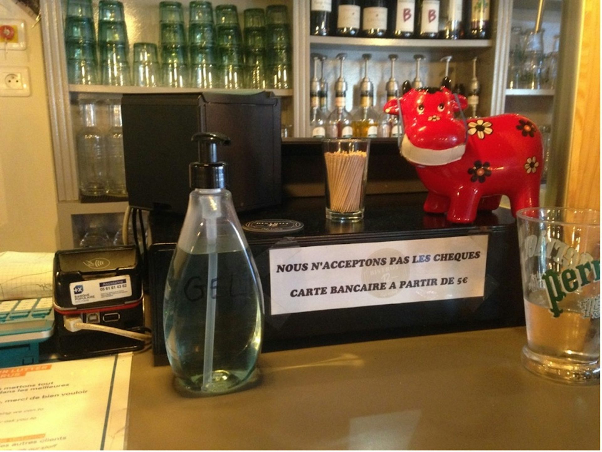 Caisse dans un bar avec écrit « Nous n'acceptons pas les chèques. Carte bancaire à partir de 1 euro ».