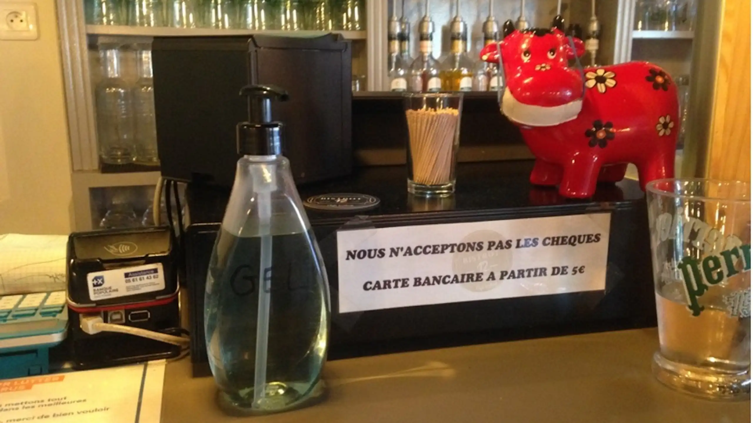 Caisse dans un bar avec écrit « Nous n'acceptons pas les chèques. Carte bancaire à partir de 1 euro ».