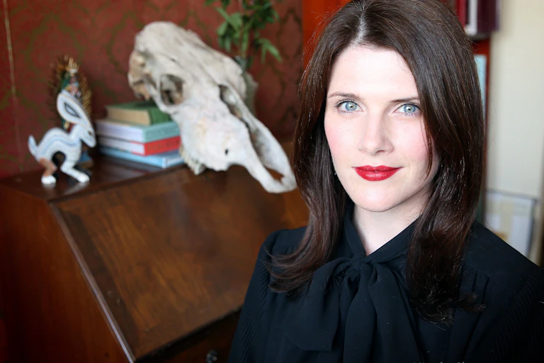 a young woman with dark hair and red lipstick, a skull behind her