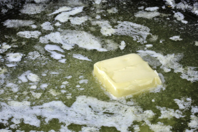 A square pat of margarine melting in a pan