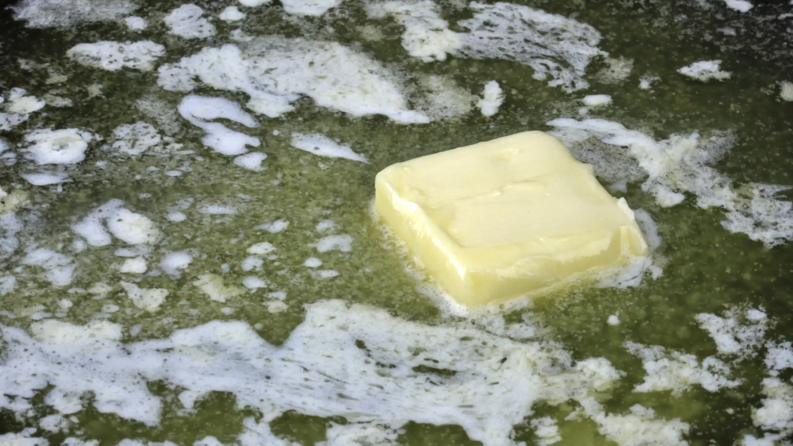 A square pat of margarine melting in a pan