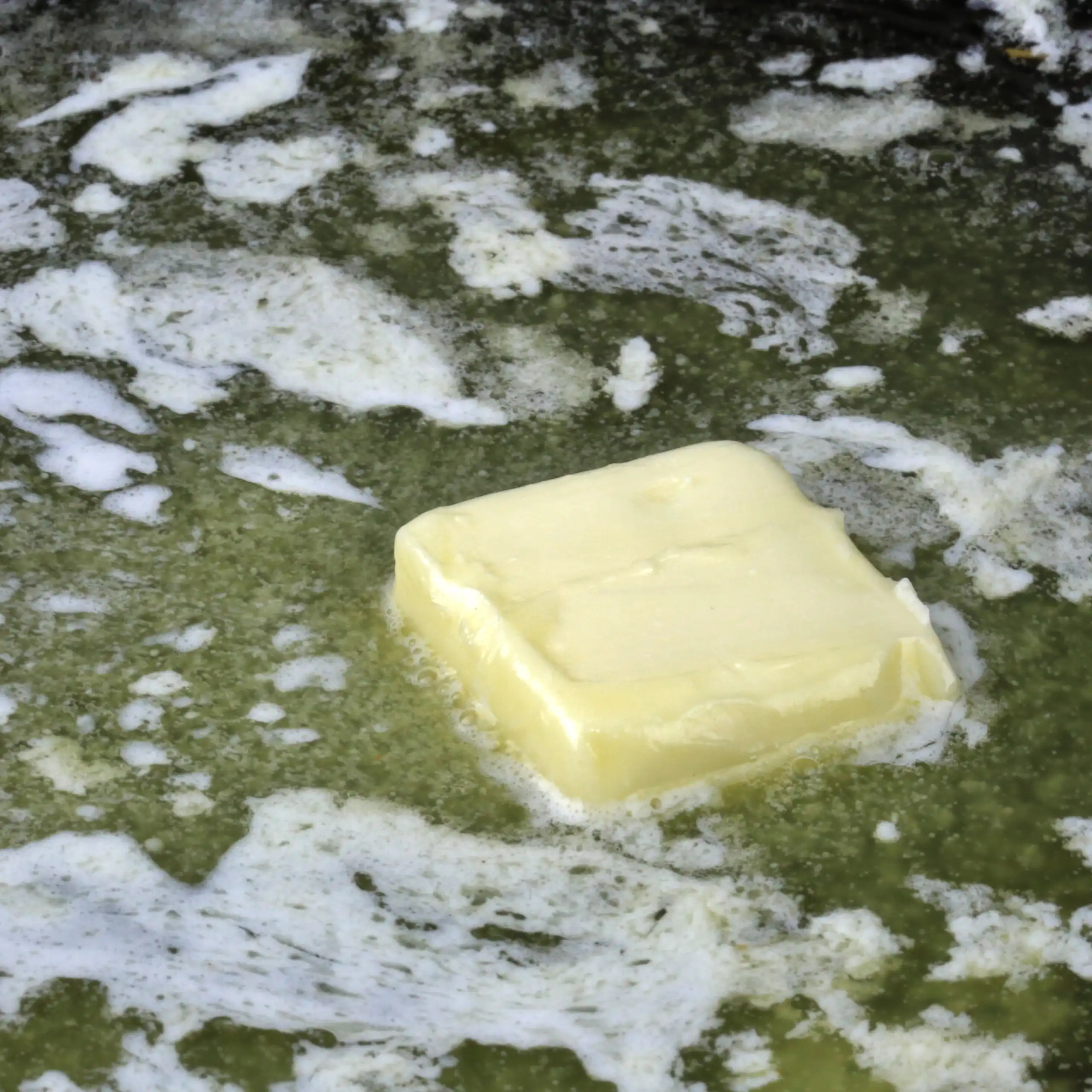 A square pat of margarine melting in a pan
