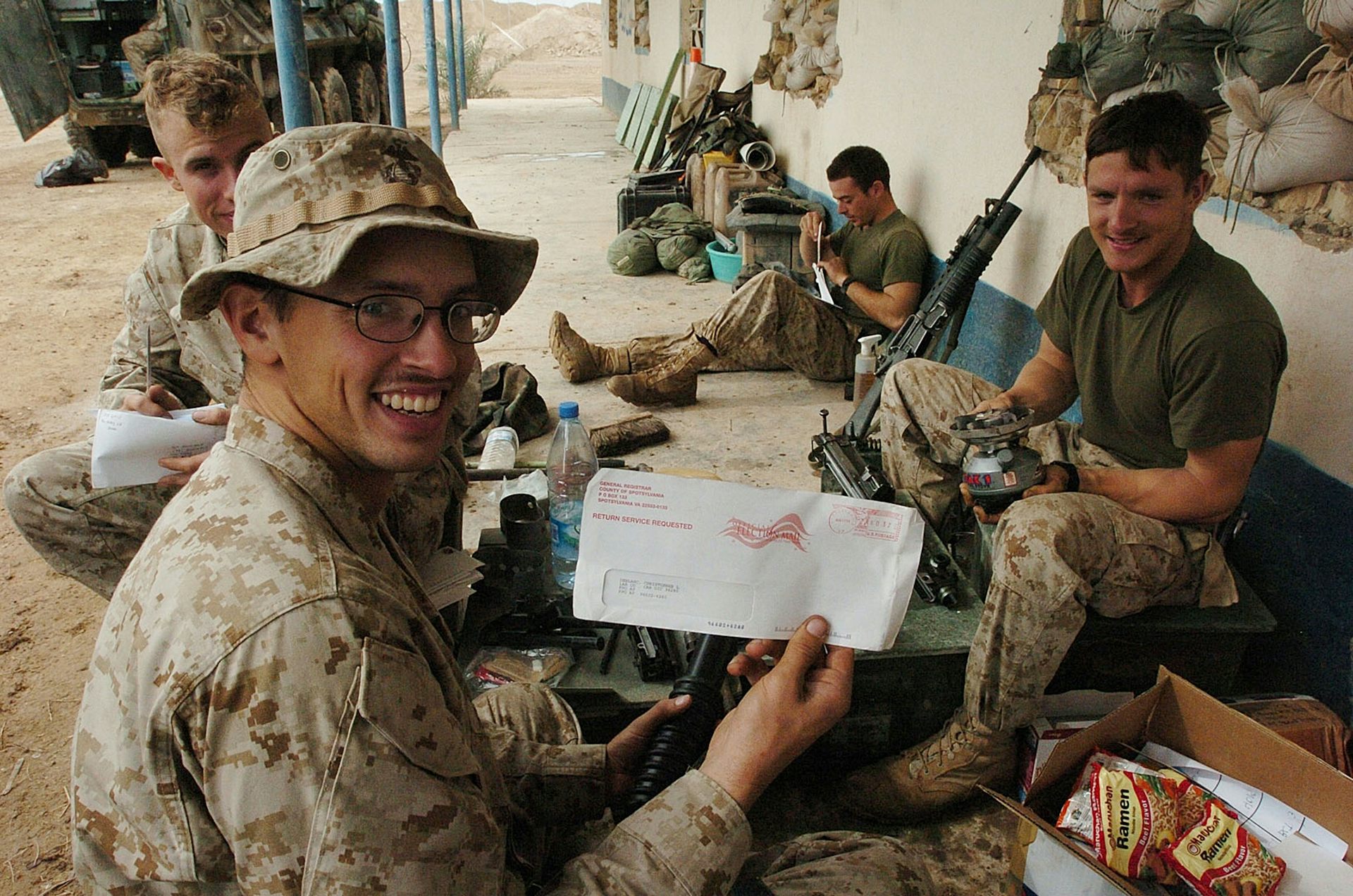 Marines in camouflage outdoors holding envelopes and election voting materials