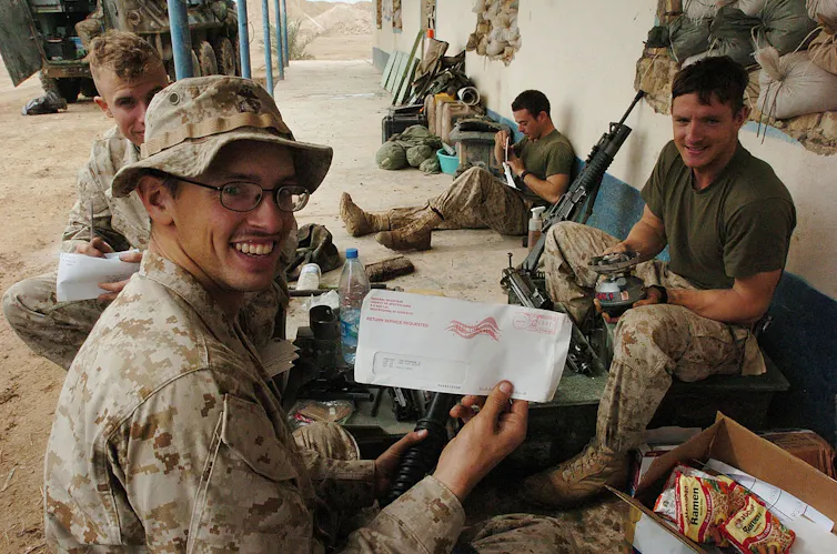 Marines in camouflage outdoors holding envelopes and election voting materials