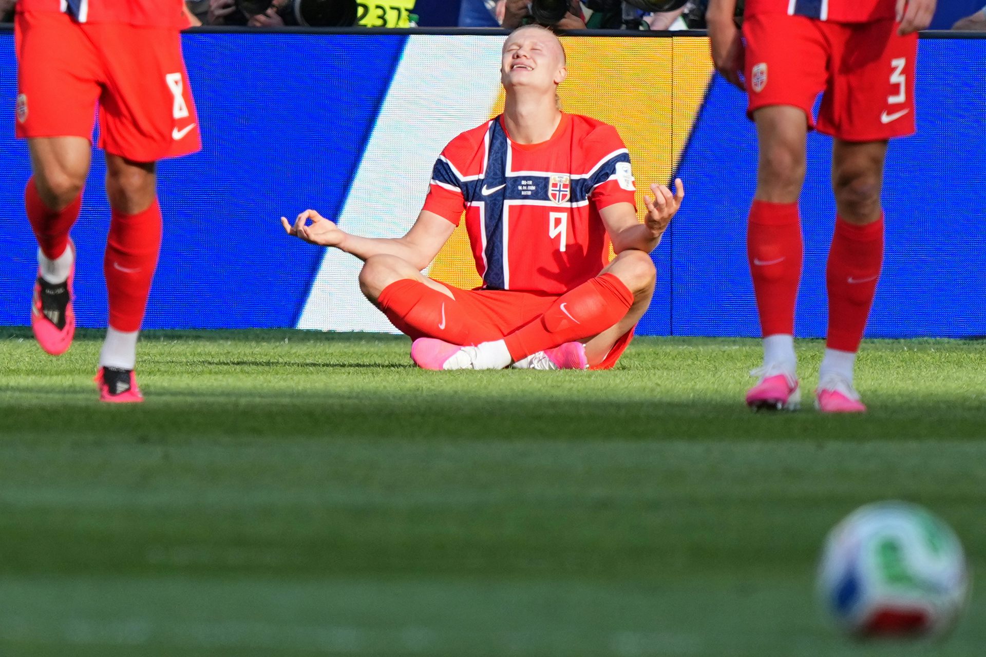 A man in a red soccer kit sits on the grass.